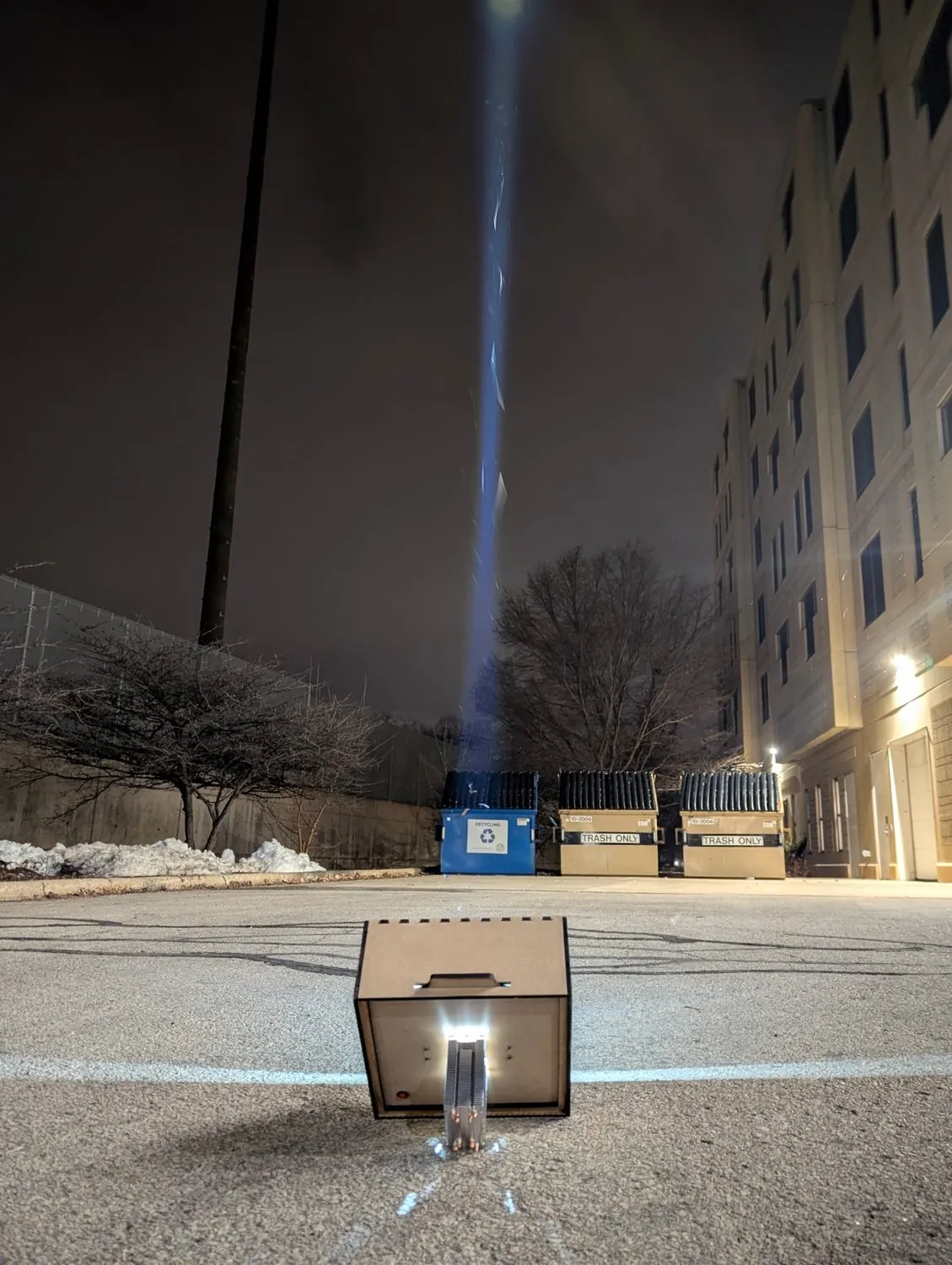 The spotlight standing on its CPU cooler in a car park at night, beam pointed straight up into the sky.